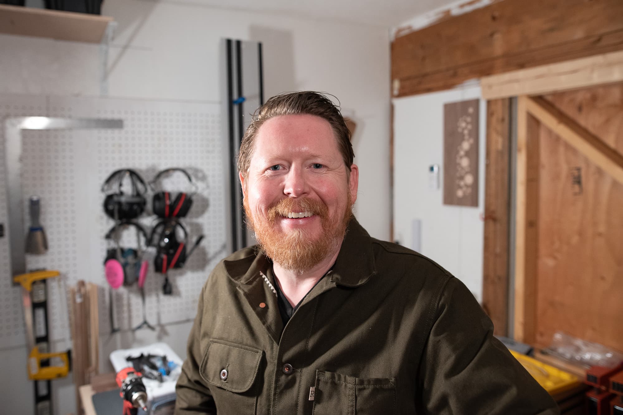 Christopher in the shop, hearing protection hung on the pegboard behind him